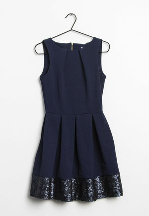 Robe bleu marine sans manches avec des plis structurés et un ourlet à sequins, suspendue sur un cintre noir sur fond blanc.