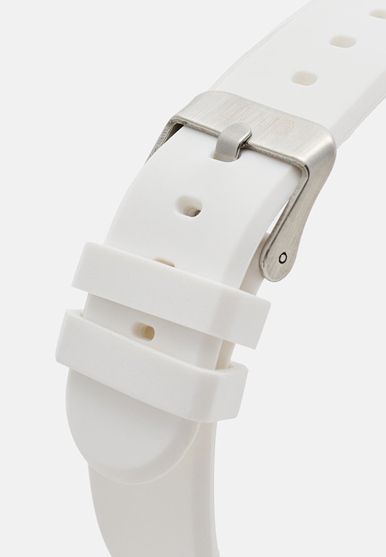 Bracelet de montre en silicone blanc avec une texture lisse, boucle en métal argenté et trous ajustables pour le dimensionnement. Comprend deux boucles de maintien.