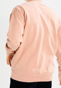 Sudadera de color rosa claro, cuello redondo, mangas largas, puños acanalados, tela de algodón suave, corte holgado, detalle de costura visible en el dobladillo.