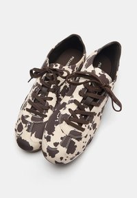Sneaker mit einem cremefarbenen Grund, braunem Kuhmuster, braunen Schnürsenkeln und runder Zehenpartie. Hergestellt aus glattem, strukturiertem Material.