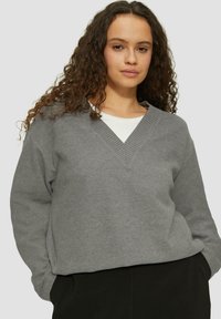 Grauer V-Ausschnitt-Sweatshirt mit geripptem Kragen, aus weichem Material, lockere Passform, getragen über einem weißen Hemd, vor einem hellen Hintergrund.