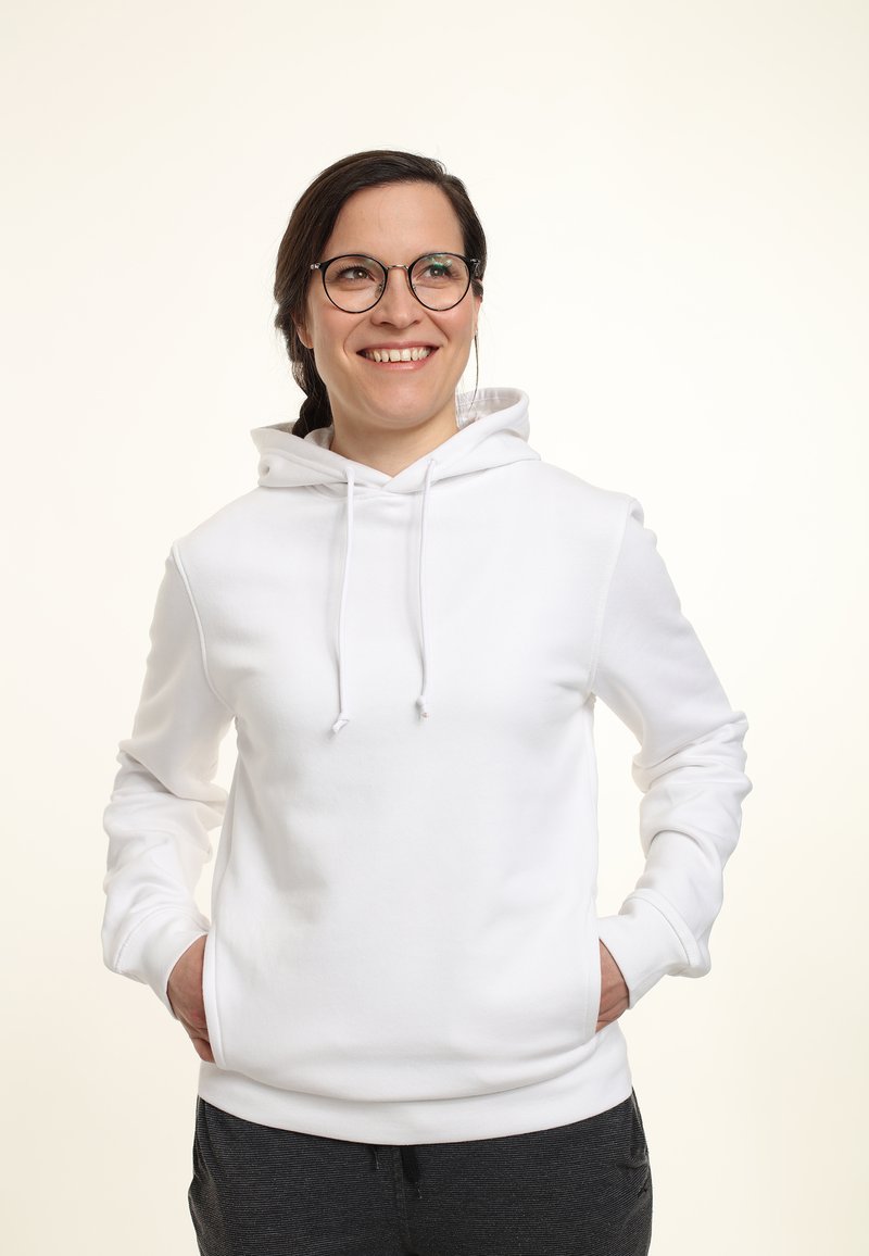 Felpa bianca con tasca frontale, cappuccio con coulisse e maniche lunghe, indossata sopra pantaloni grigio scuro. Tessuto liscio.
