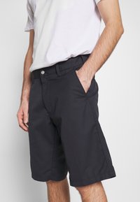 Svarta bomullsshorts med en tight design, sidfickor och en platt midja. Kombinerade med en enkel vit t-shirt.