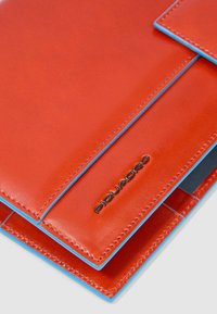 Rode leren portemonnee met blauwe stiksels, voorzien van een slank ontwerp en een metalen logo. Gladde textuur en strakke lijnen kenmerken het uiterlijk.