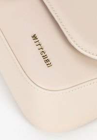 Borsa a mano in pelle beige con una texture liscia, caratterizzata da un flap arrotondato, bordi cuciti e un logo in rilievo dorato, "WITTCHEN."
