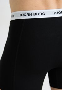 Uvećanje osobe koja nosi crne bokserice s bijelim pojasom na kojem je brend "BJÖRN BORG" ispisan crnim tekstom.