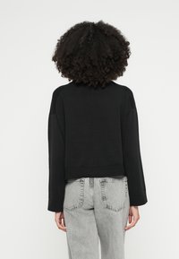 Melna īsā džemperis ar maigu tekstūru, raglāna piedurknēm un ribainu apakšu. Pievienotas gaiši pelēkas, augstu jostasvietu bikses.