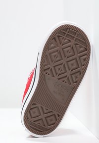 Rode canvas sneakersole met een gestructureerde bruine rubberen loopvlak. Heeft een witte rubberen bumper en een zwarte streep langs de rand. "Converse All Star" branding zichtbaar.