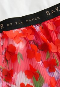 Falda plisada floral que presenta una combinación vibrante de colores rosa y rojo, adornada con apliques tridimensionales de flores rojas y una pretina negra con la marca.