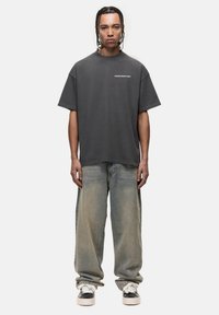 Przesadna, ciemnoszara bawełniana koszulka z krótkim rękawem i okrągłym dekoltem, zestawiona z jasnoniebieskimi, luźnymi dżinsami i czarnymi sneakersami.