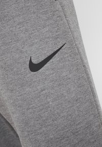 Šedé sportovní kalhoty vyrobené z měkké tkaniny, s černým logem Nike na stehně a jednoduchým, aerodynamickým designem.