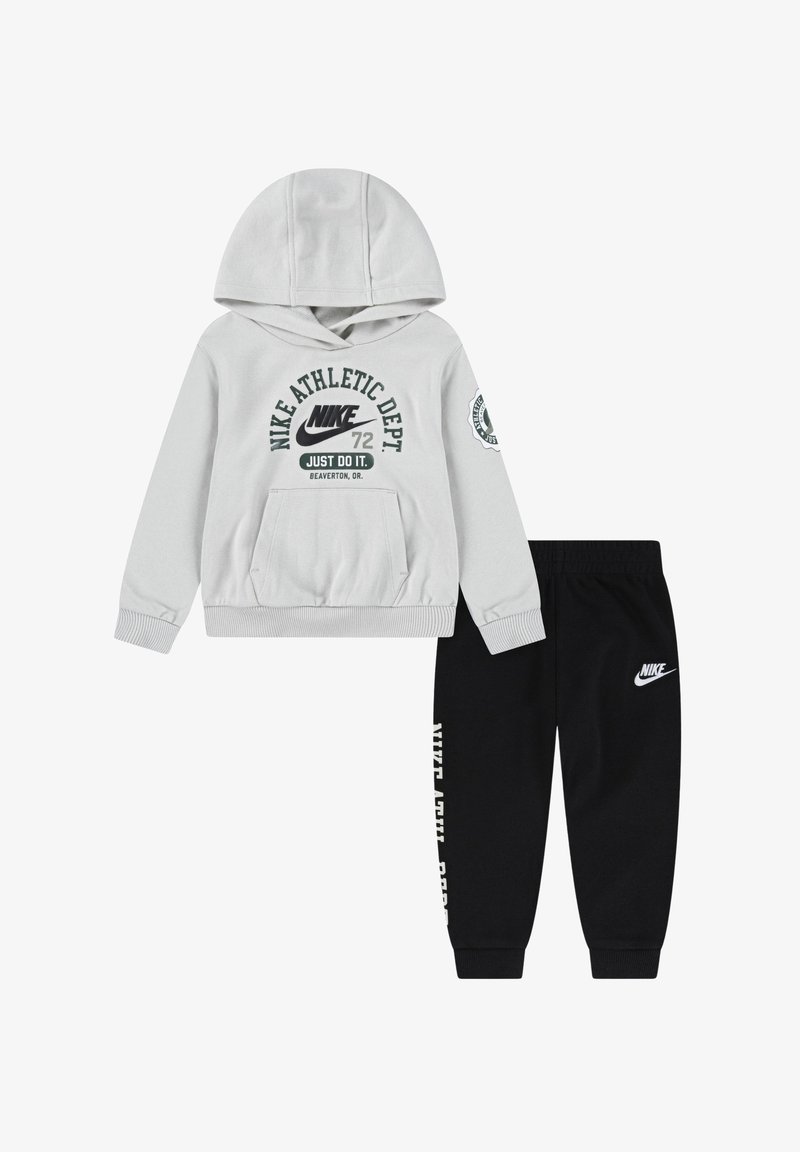 Sudadera gris con bolsillo frontal y texto gráfico, combinada con pantalones jogger negros que tienen un logo y texto en el lado. Ambos son de mezcla de algodón.