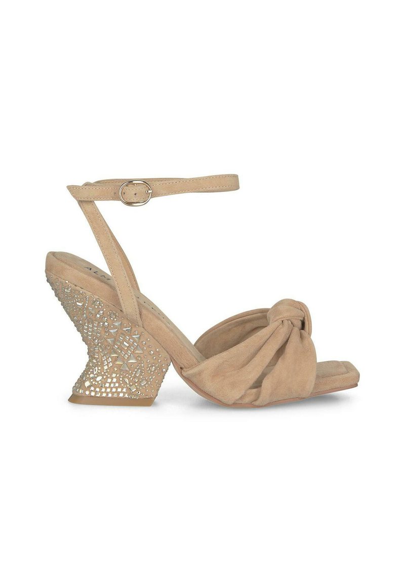 Sandali beige in suede con zeppa, fronte annodato, cinturino alla caviglia regolabile e una base metallica con pattern per aggiungere texture e dettaglio.