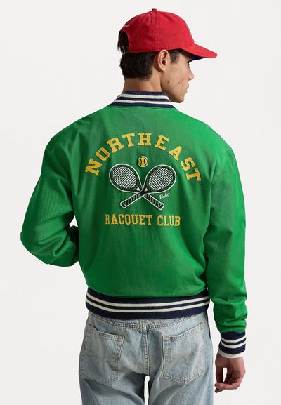 Zaļš bomber jackets ar baltām un tumši zilām svītrām pie piedurknēm, ar dzeltenu izšuvumu "NORTHEAST RACQUET CLUB" un krustotiem tenisa raketēm.