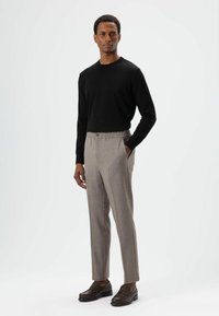 Zwart shirt met lange mouwen gecombineerd met lichtgrijze, op maat gemaakte broek met elastische tailleband en een enkele knoop. Bruine instapschoenen.