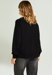 Suéter negro de punto con ajuste holgado, con mangas abullonadas y detalles decorativos de botones en los puños. Textura suave, dobladillo acanalado.