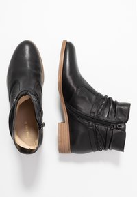 Botas de cuero negras hasta el tobillo con un tacón bajo, cremallera lateral y detalles fruncidos. Textura suave con un acento de tacón de madera.