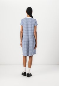 Gestreiftes T-Shirt-Kleid in Blau und Weiß, mit kurzen Ärmeln, einem gerafften Bund und einem knielangen Saum. Getragen mit schwarzen Schuhen und weißen Socken.