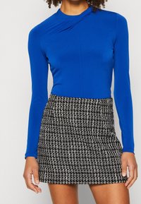 Blå långärmad topp med en smal passform och subtil drapering, kombinerad med en svart och vit texturerad minikjol.