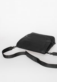 Black crossbody bag with adjustable strap, rectangular shape, and subtle embossed logo on smooth fabric surface.