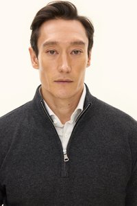 Dunkelgrauer, mit Reißverschluss versehener Pullover mit glatter Textur, der einen hohen Kragen und ein darunter liegendes weißes Hemd aufweist. Auffällige silberne Reißverschlussbeschläge.