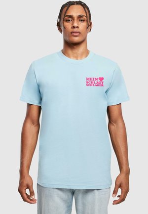 Lyseblå bomulds t-shirt med pink tekst "MEIN ♥ SCHLÆGT SCHLAGER" på venstre bryst. Korte ærmer og klassisk rund halsudskæring.