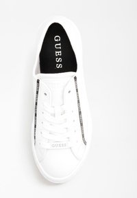 Sneaker bianca Guess con soletta nera, stringhe bianche e strisce laterali nere con il logo "GUESS" ripetuto.
