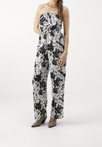 Jumpsuit floral en blanco y negro con un top sin tirantes, cintura elástica, pantalones de pierna ancha y tela suave. Combinado con tacones de punta.