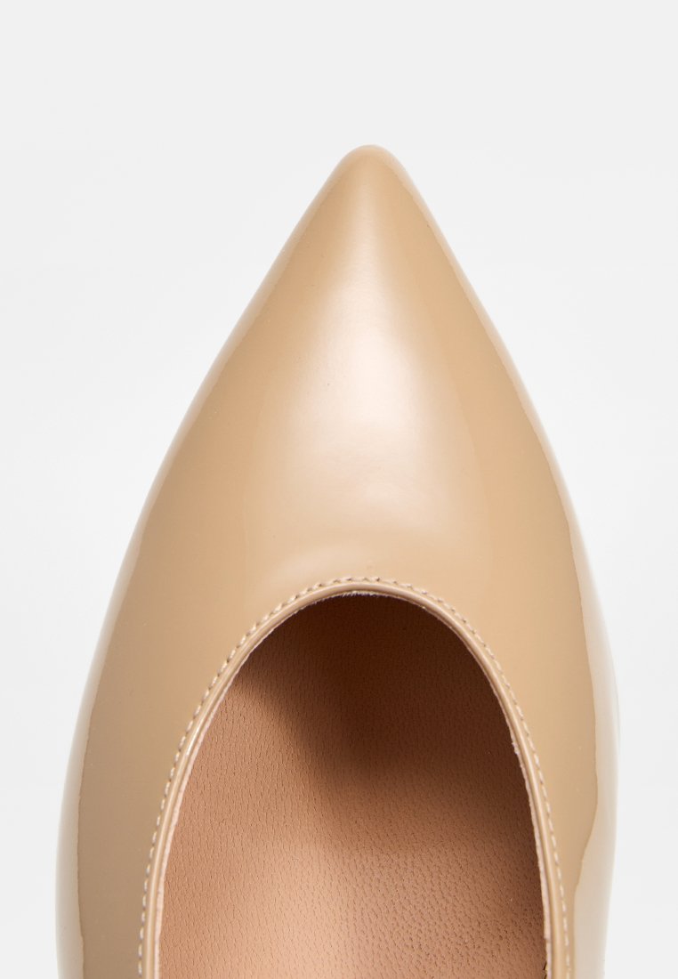 Pump in pelle verniciata beige con punta a forma appuntita, superficie liscia, silhouette elegante e bordo scallopato attorno all'apertura.