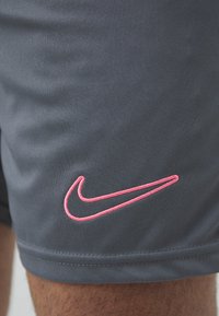 Shorts de sport gris en tissu texturé, avec un logo Nike brodé en rose sur le bas à gauche. Ourlet cousu.