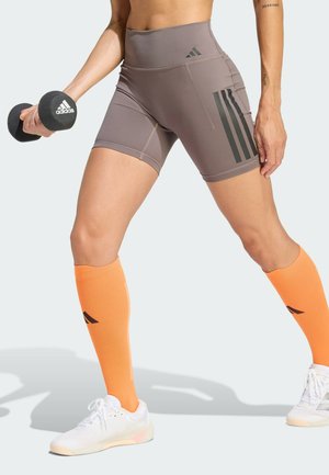Gray high-waisted shorts with black stripes, paired with orange knee-high socks and white sneakers, holding a black dumbbell.