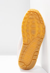 Light-colored athletic shoe sole with a textured yellow rubber grip pattern and logo detailing, showing a smooth transition from heel to toe.