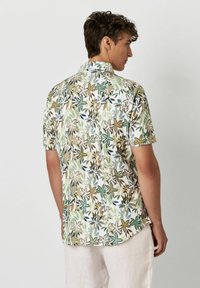 Das kurz�ärmelige Hemd weist ein florales Muster in Grün, Gelb und Schwarz auf einem weißen Hintergrund auf. Hergestellt aus leichtem Stoff mit einem lockeren Schnitt.