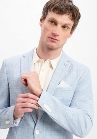 Hellblaues kariertes Blazer mit Reverskragen, weißen Knöpfen und einem weißen Taschentuch in der Brusttasche; kombiniert mit einem cremigen Hemd.