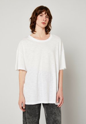 T-shirt en coton blanc oversize avec un col rond, des manches courtes et une coupe décontractée, présentant un tissu doux et légèrement texturé.