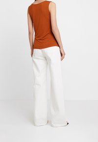 Top ruggine senza maniche abbinato a pantaloni bianchi a vita alta con gamba larga. Il tessuto appare morbido, con un design pulito e minimale e senza decorazioni.