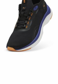 Basket de sport pour homme noire et violette avec des touches orange, semelle blanche et logo Puma au talon et à la languette, inclinée pour montrer l'avant et le côté.