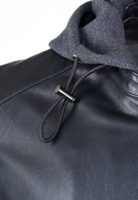 Sort læderjakke med en grå fleece-betrukket hætte, justerbar snøre og metalliske hardwareakcenter. Glat tekstur over hele jakken.