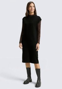 Czarna sukienka bez rękawów o prostym kroju, zestawiona z długim topem w panterkę pod spodem. Noszona z czarnymi kozakami za kolano.