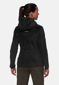Giacca in pile nera con finitura strutturata, design con cappuccio e logo sulla parte posteriore. Maniche lunghe e tasche con zip.