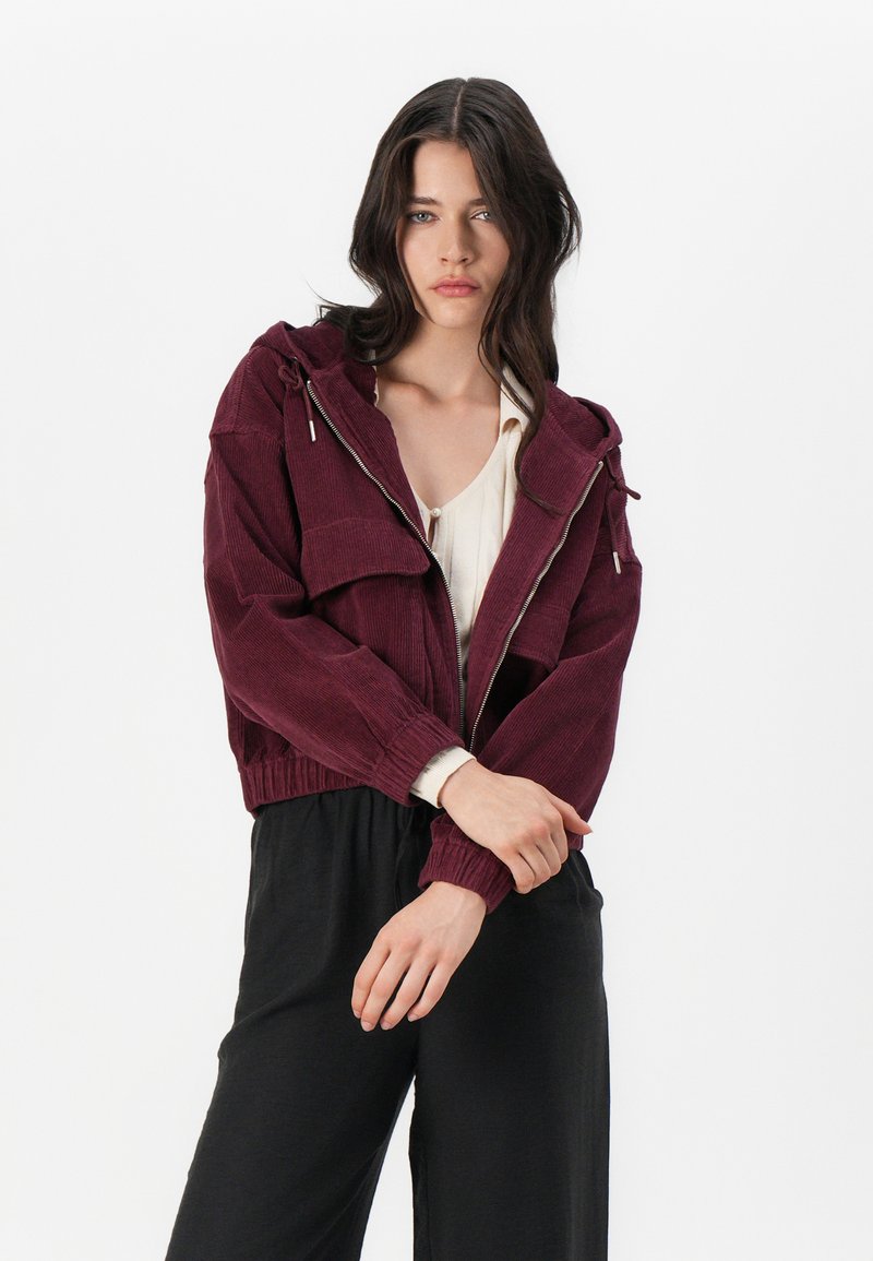 Burgundowa, krótkia kurtka z kordurowego materiału, z kapturem, z przodu na zamek i ściągaczami przy mankietach. Łączona z jasnym topem i czarnymi spodniami.