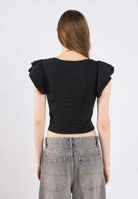 Top corto negro de canalé con mangas cortas y con volantes, combinado con jeans de pierna ancha gris claro que cuentan con dos bolsillos traseros y detalles de costura visibles.