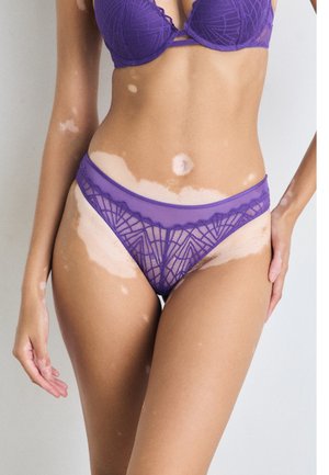 Fialová souprava spodního prádla obsahující podprsenku se geometrickými vzory a odpovídající bikiny. Měkká látka se zdobením z průsvitné krajky podél okrajů.