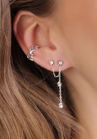 Pendiente en forma de estrella plateada, con un cuff y aretes que incluyen elementos de cadena, adornados con acentos facetados y un acabado pulido. Diseño texturizado y contemporáneo.