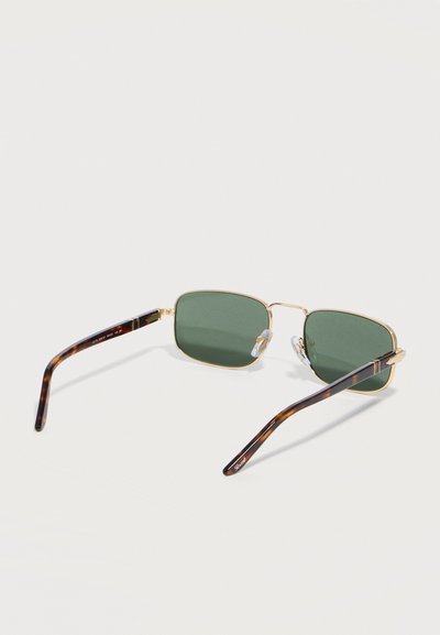 Ορθογώνια γυαλιά ηλίου με χρυσή κορνίζα, σκουρόχρωνους πράσινους φακούς και βραχίονες με σχέδιο από γαρίδα χελώνας, ακουμπισμένα σε λευκή επιφάνεια.