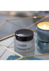 Crème de nuit unifiante AHAVA Age Control dans un pot en verre dépoli avec un couvercle noir, comportant un texte en relief et une surface lisse et brillante.