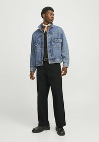 Lysblå denimjakke med to forlommer, krave og knaplukning, parret med sorte vide bukser og kraftige sorte sko.