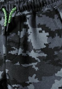 Pantaloni jogger mimetici grigi realizzati in un tessuto morbido, dotati di un cordoncino con dettagli verdi e una superficie testurizzata.