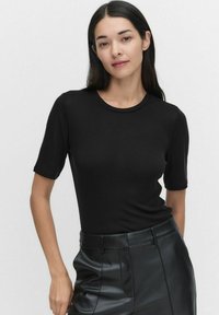 Zwarte T-shirt met korte mouwen, gemaakt van rekbaar materiaal, met een ronde halslijn en een getailleerde pasvorm. Gecombineerd met high-waisted leren broek.