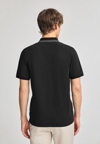 Svart polo tröja med en tvåknappslång, korta ärmar och en texturerad tyg. Har en kontrasterande grå rand längs kragen.